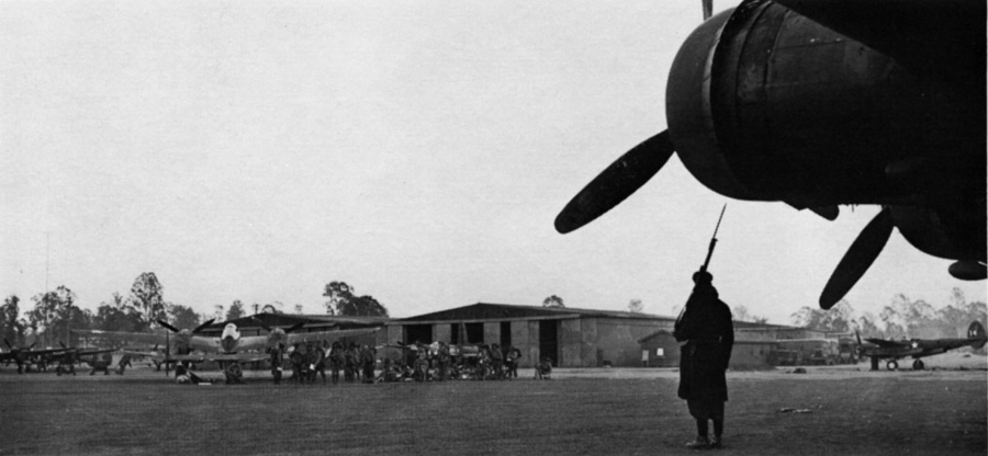 An Australian sentry guards an American Boeing B–17 ‘Flying Fortress’ in the early morning as Soldiers of the 128TH Infantry, 32D Division, wait in the distance to board a plane for New Guinea at Amberly Field, Ipswich, Australia, on 18 September 1942.