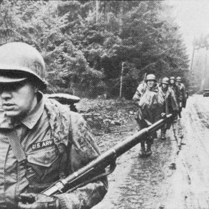 32D Inf. Div. Soldiers conduct a tactical march along a muddy road in the rain during training at Fort Lewis, WA, ca. ’61-’62.